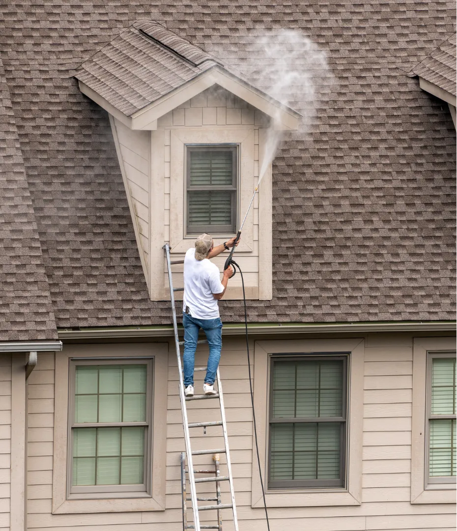 Man on ladder pressure washing gutter